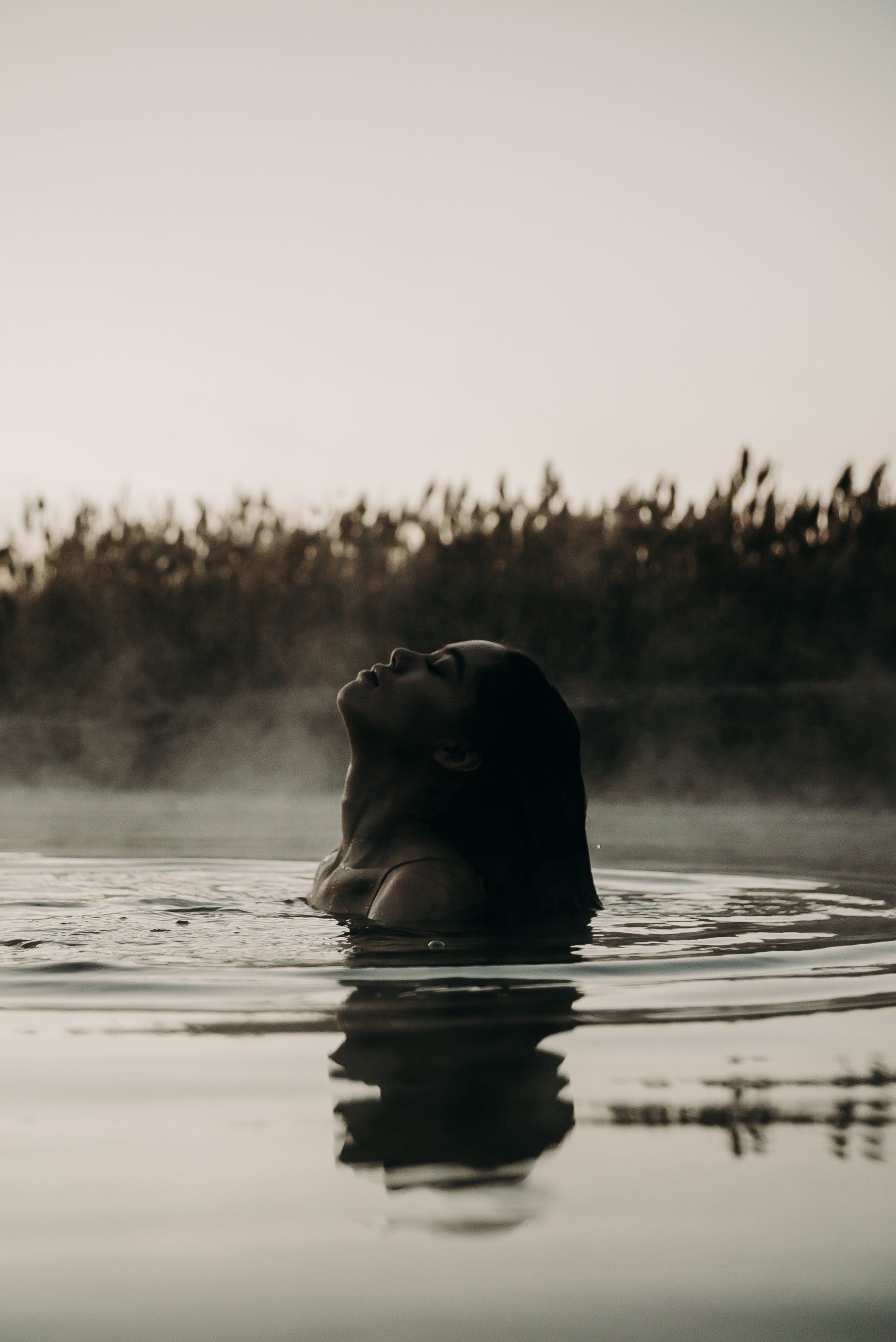A woman is swimming in a lake with her head above the water.