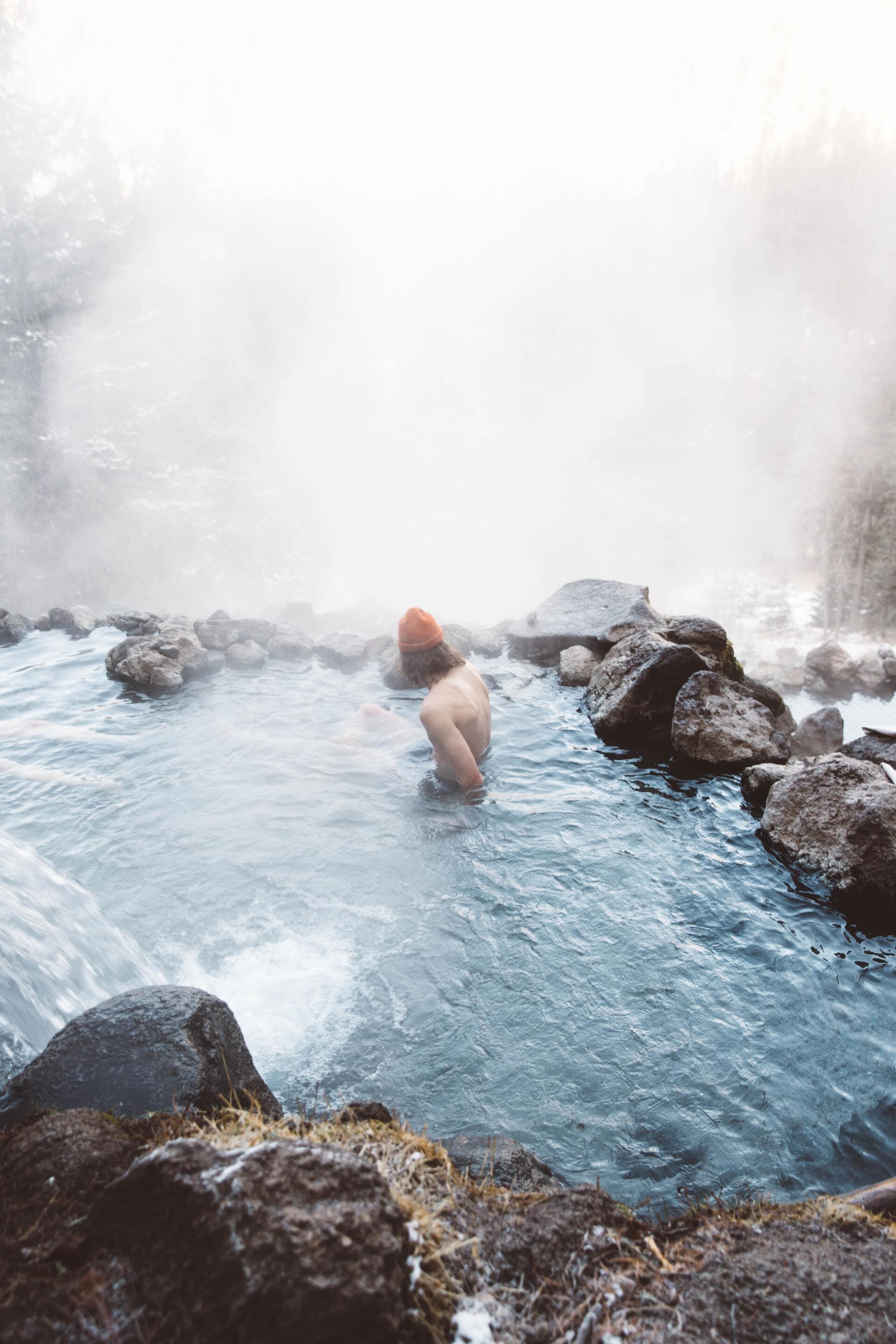 A man is swimming in a hot spring surrounded by rocks.