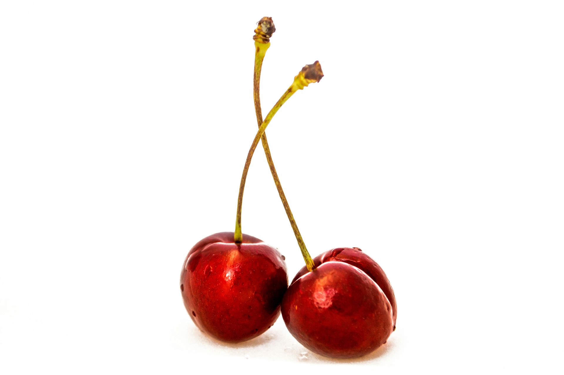 Two bright red cherries with green stems connected at the top, isolated against a white background.