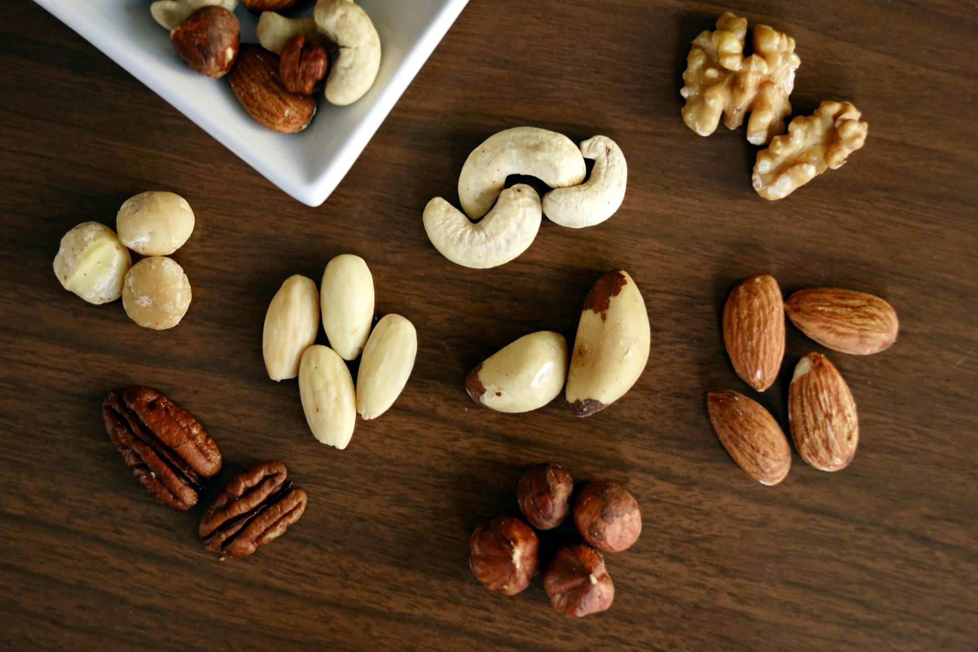An assortment of raw nuts including walnuts, cashews, almonds, pecans, and hazelnuts arranged on a wooden surface.
