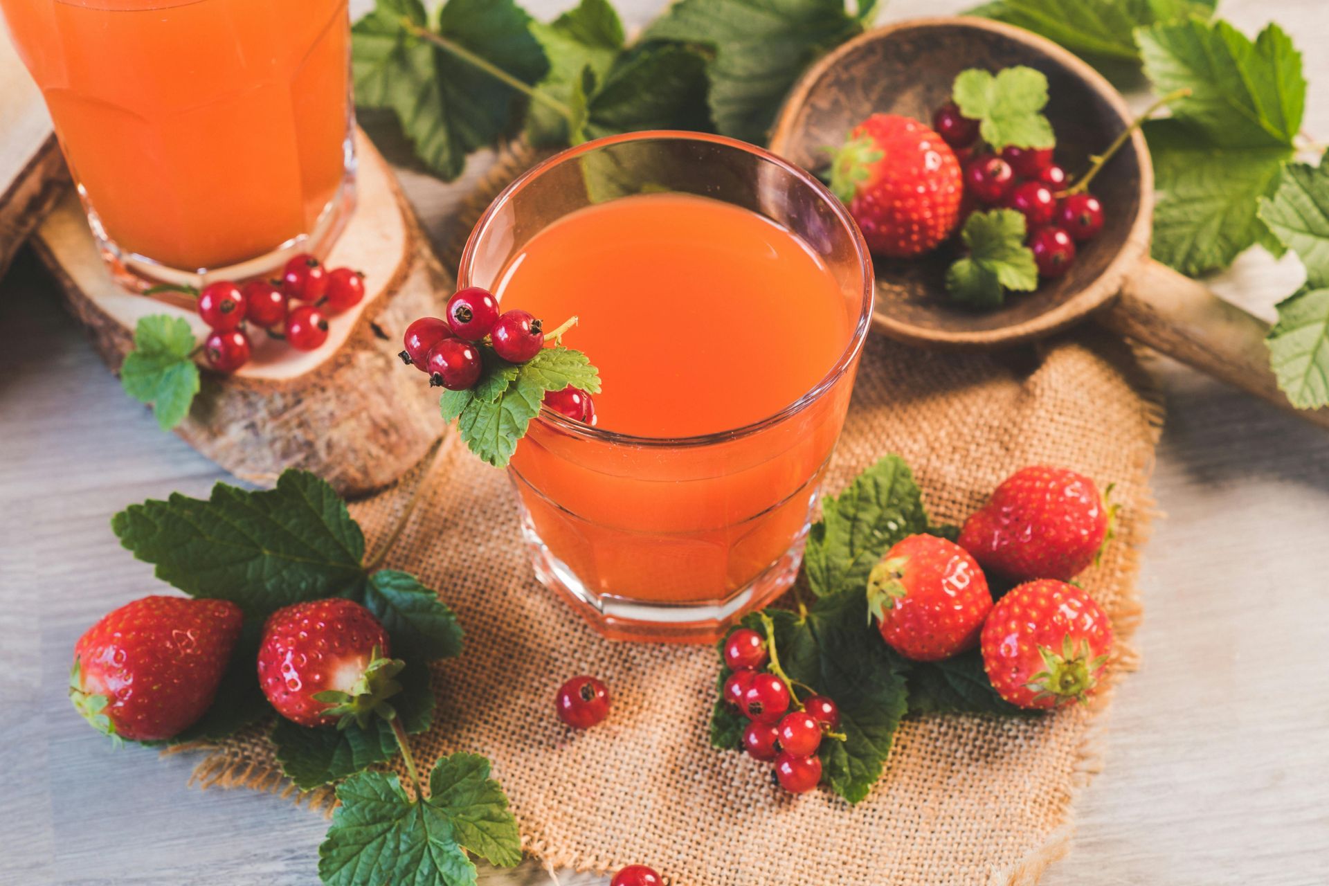Two glasses of orange juice garnished with red currants and strawberries on a wooden surface with scattered berries.