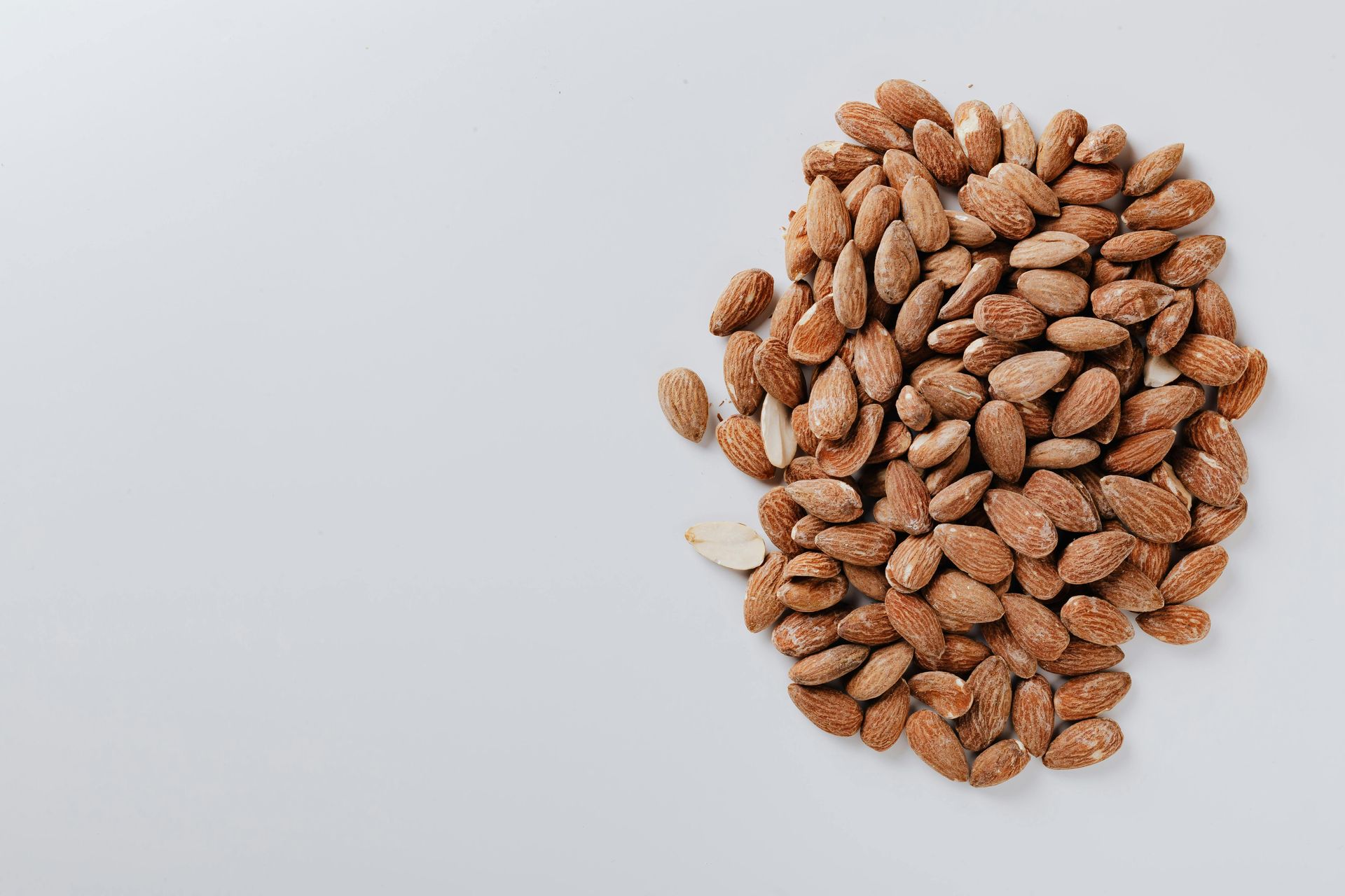 A pile of cinnamon-coated roasted almonds centered on a plain, light grey background.