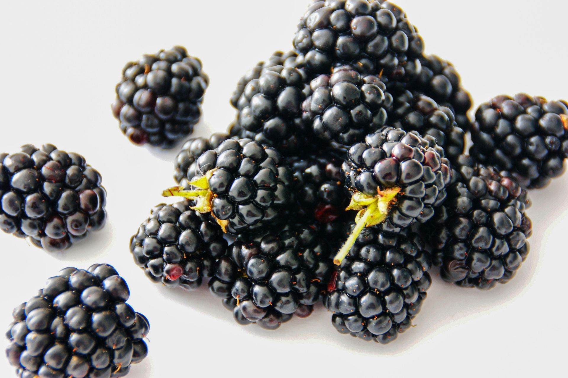 A small pile of dark, ripe blackberries against a plain white background, with a few scattered berries to the side.