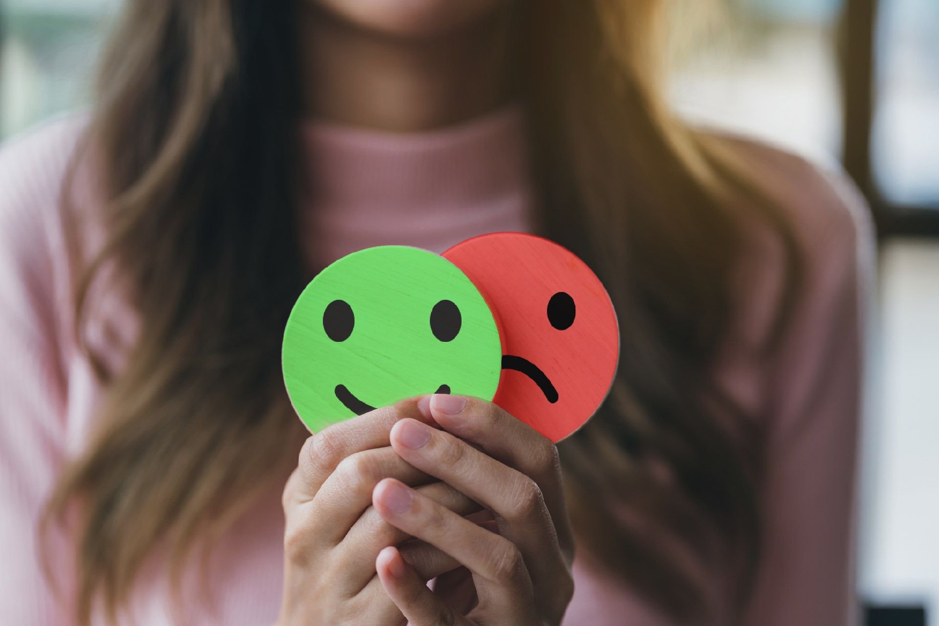 Mujer sosteniendo un recorte de una cara feliz verde y una cara triste roja.