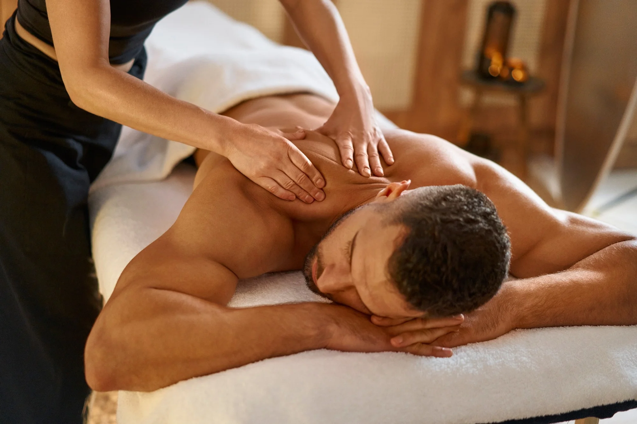 Spa massage therapist rubbing a client’s back on a treatment table, with candles in the background