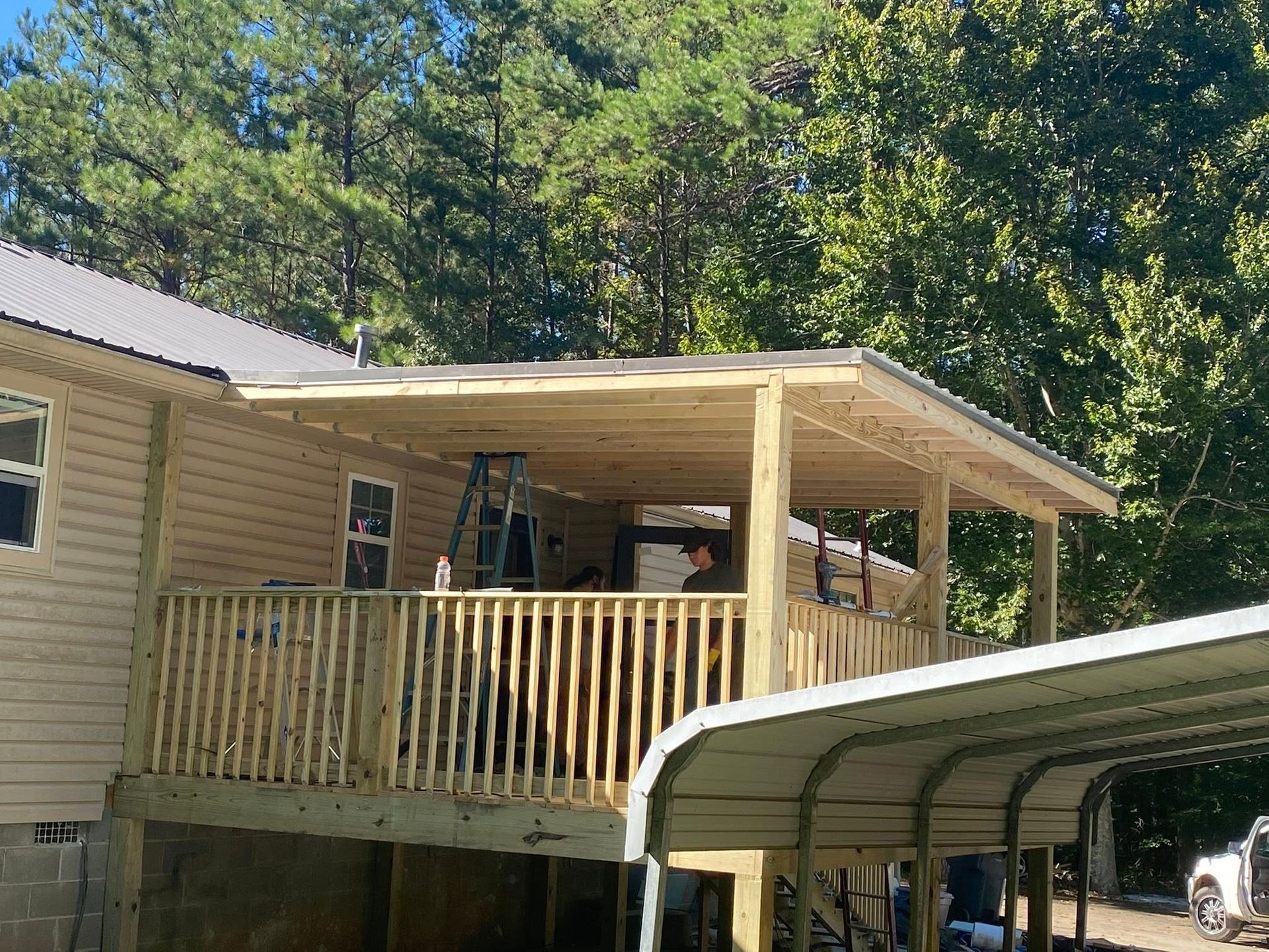 A new wooden deck attached to a house with a metal roof, surrounded by trees.