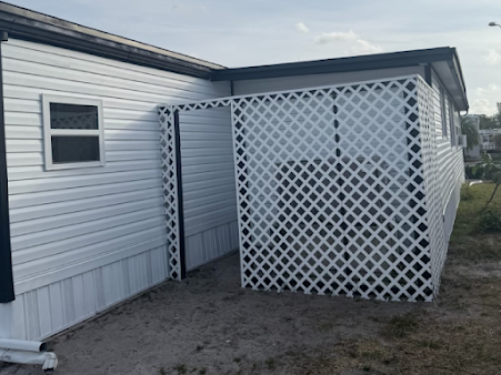 White latticework enclosure attached to a white-sided building, creating a small outdoor space.