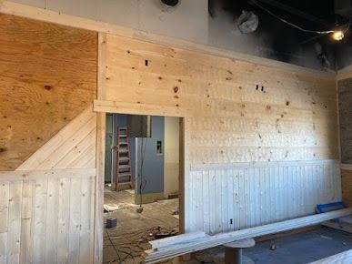 Interior wall construction with wood paneling, door frame, and plywood, showing a building in progress.