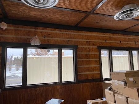 Interior with log walls, windows, and ceiling vents. Boxes in the foreground, snow outside.