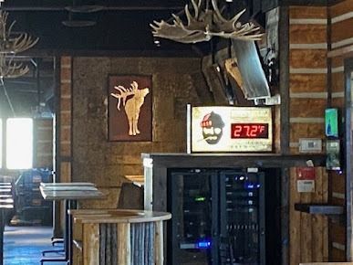 Rustic bar interior with moose decor, a temperature display, and server racks.