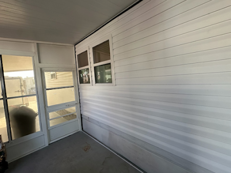 Enclosed porch with white siding, windows, and a screen door. Grey floor and ceiling.