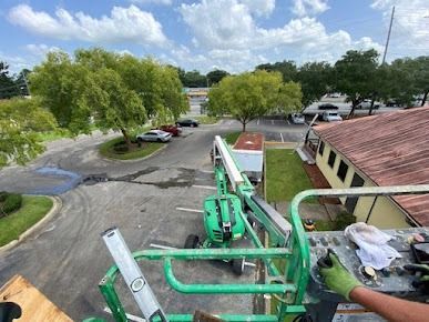 Green lift platform, operator's gloved hand, trees, parking lot, cloudy sky.