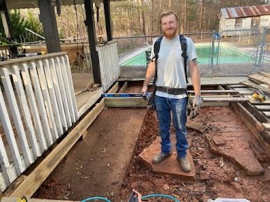 Man on deck construction site, holding a tool, in front of a pool.