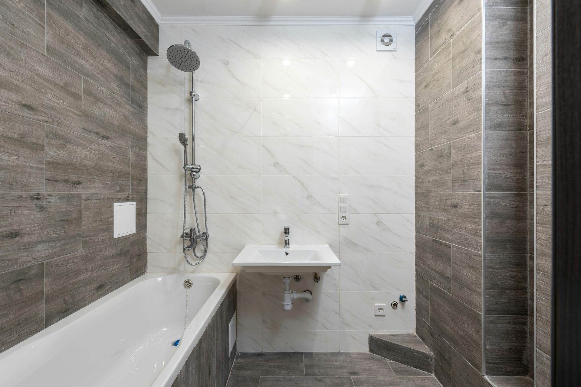 Bathroom with white bathtub, sink, and shower; gray and white tiled walls.