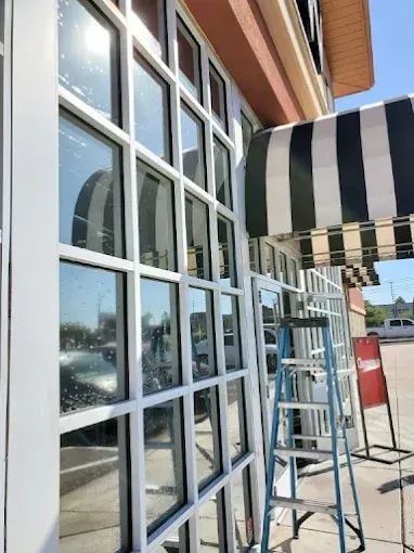 Storefront with large windows, black-and-white striped awning, and a blue ladder on the sidewalk.