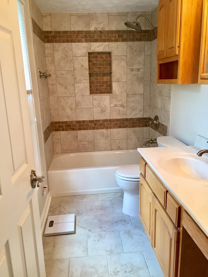 Bathroom with a tiled bathtub shower combo, toilet, light wood vanity, and a scale on the floor.