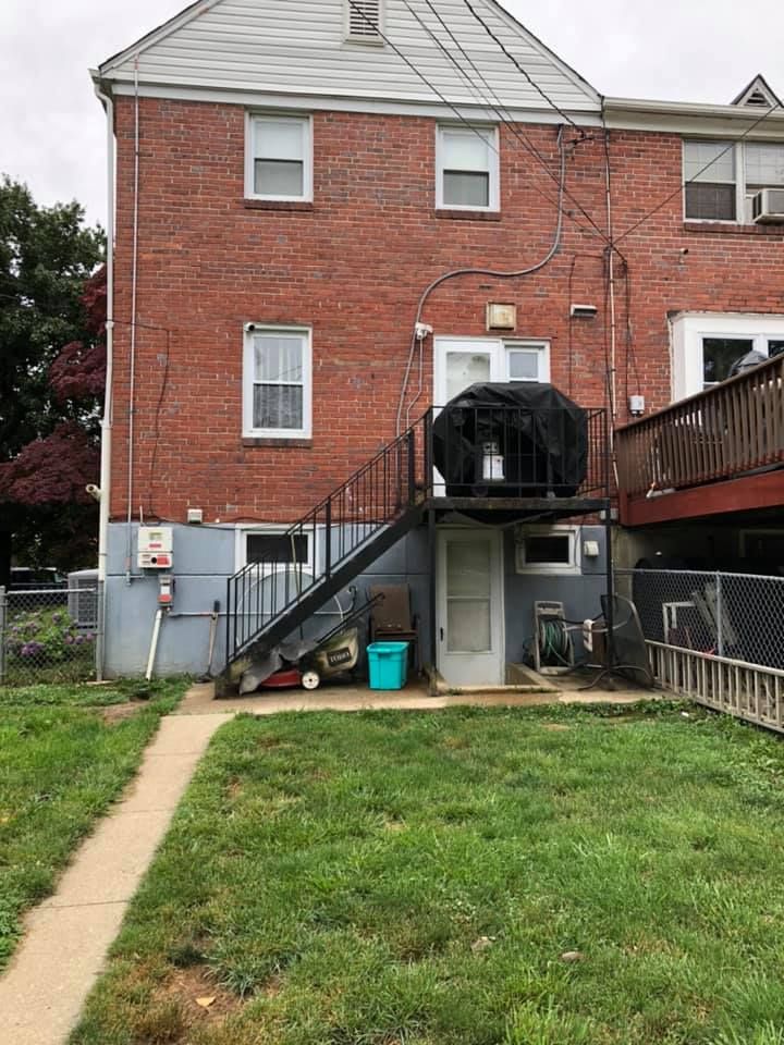 Rear view of a brick house with a metal staircase leading to an elevated back door, a patio area, and a fenced yard.