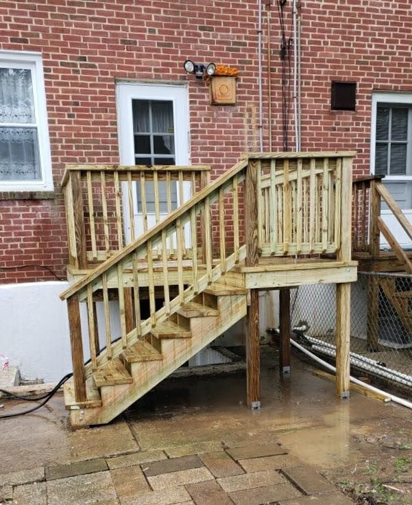 A newly constructed wooden deck and staircase installed against a red brick exterior wall.