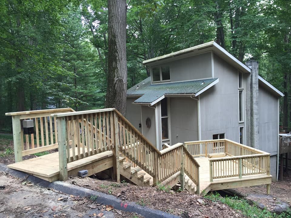 A modern gray house in a wooded area with a newly constructed wooden deck and stairs leading to the entrance.
