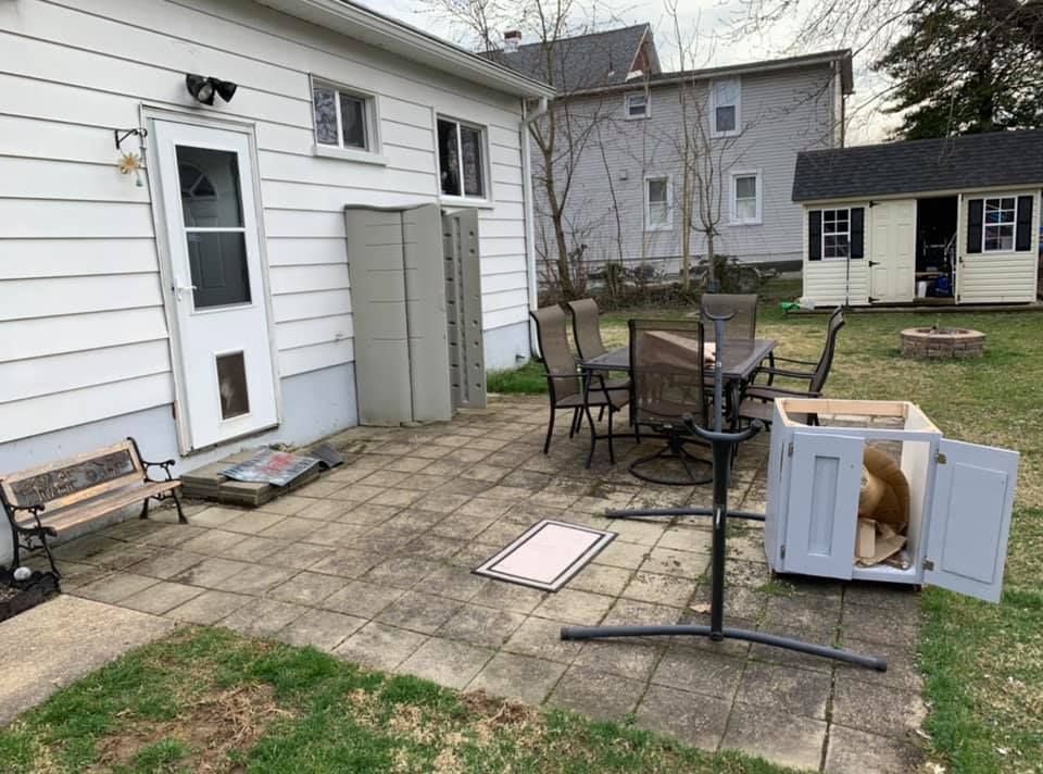 A patio with a table, chairs, a small bench, a storage cabinet, and a pet crate with a dog resting inside.