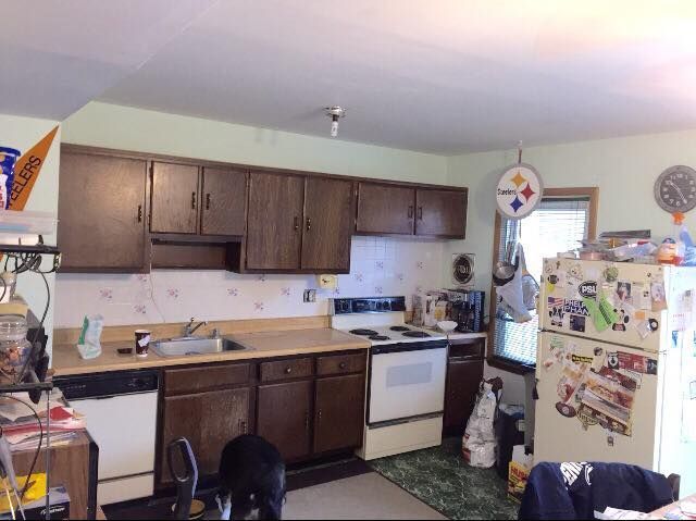 A kitchen with brown wooden cabinets, a sink, a white stove, and a refrigerator covered in magnets and stickers.