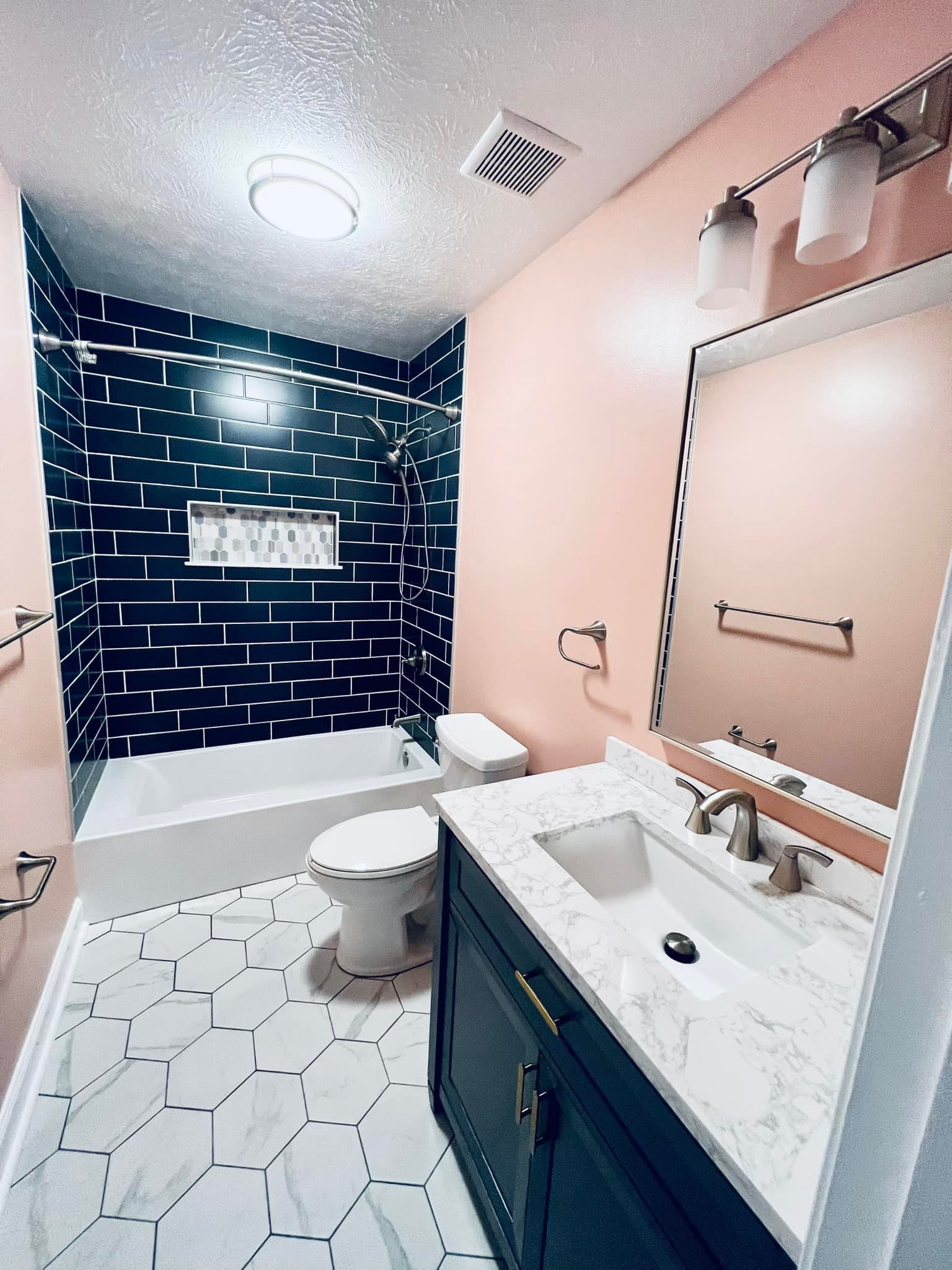 Modern bathroom with a Pac-Man maze-themed dark shower wall, pink walls, marble hexagon floor, and a dark navy vanity.