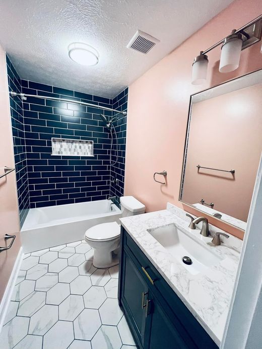 Modern bathroom with a Pac-Man maze-themed dark shower wall, pink walls, marble hexagon floor, and a dark navy vanity.