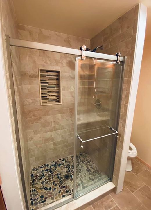Walk-in shower with stone tile walls, a pebble floor, a built-in shelf, and a glass sliding door.