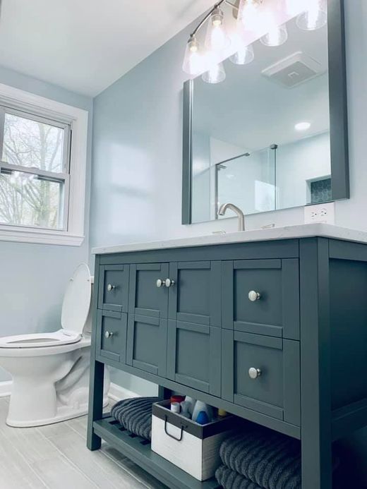 A bathroom with a dark gray vanity, a white countertop and sink, a rectangular mirror, and a toilet under a window.