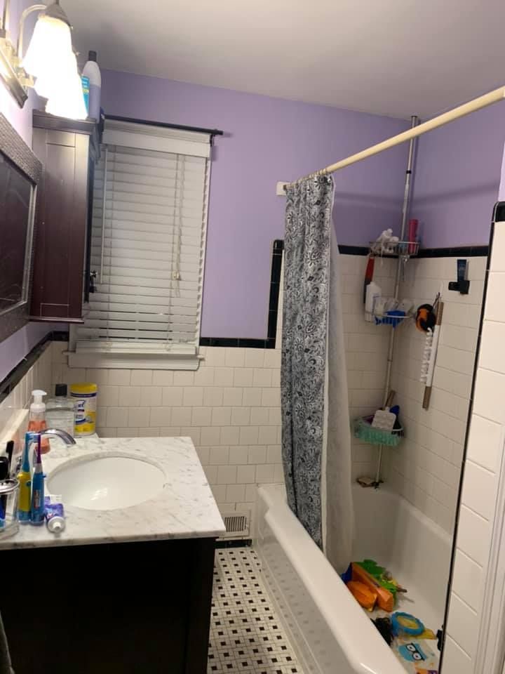 A bathroom with a dark vanity, marble countertop, purple walls, black tile accents, and a tub with a gray shower curtain.