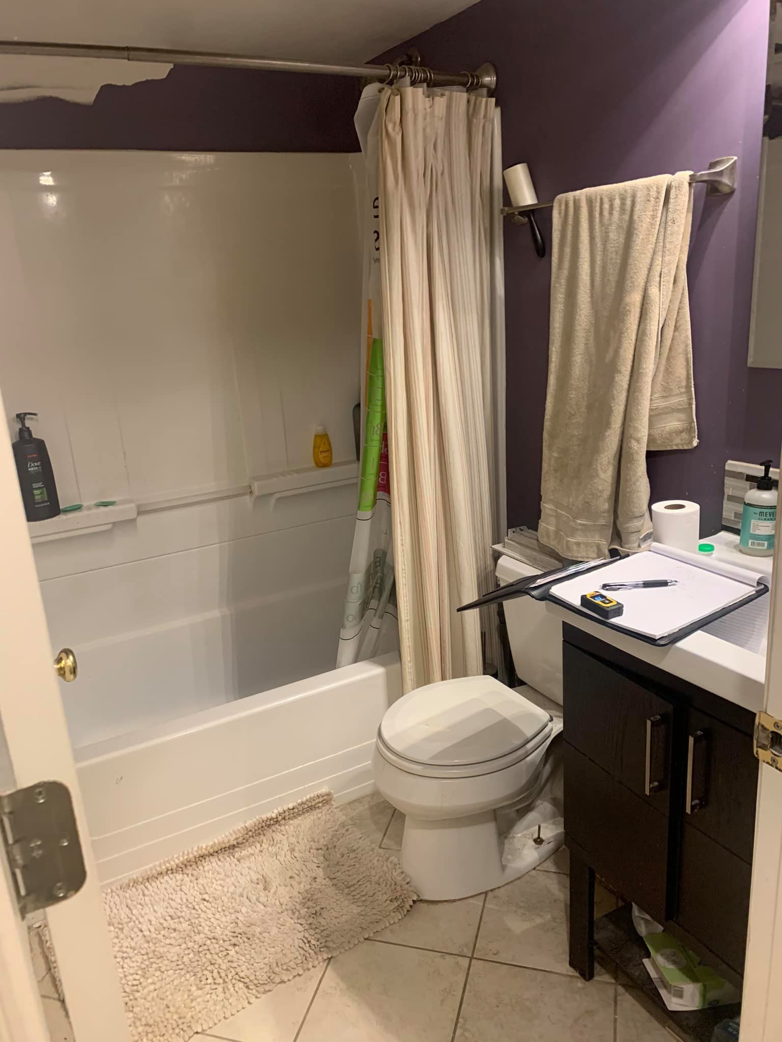 A small bathroom with a bathtub, toilet, and dark brown vanity cabinet against purple walls.