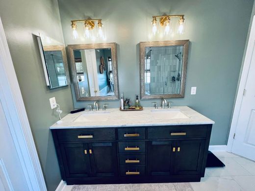 A double vanity with a dark wood cabinet, marble countertop, two mirrors, and brass light fixtures on a sage green wall.