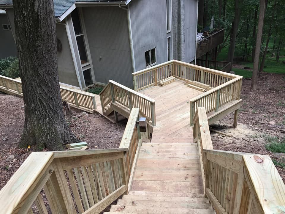 Wooden outdoor staircase with railings leading down from a house to a wooden deck in a wooded yard.