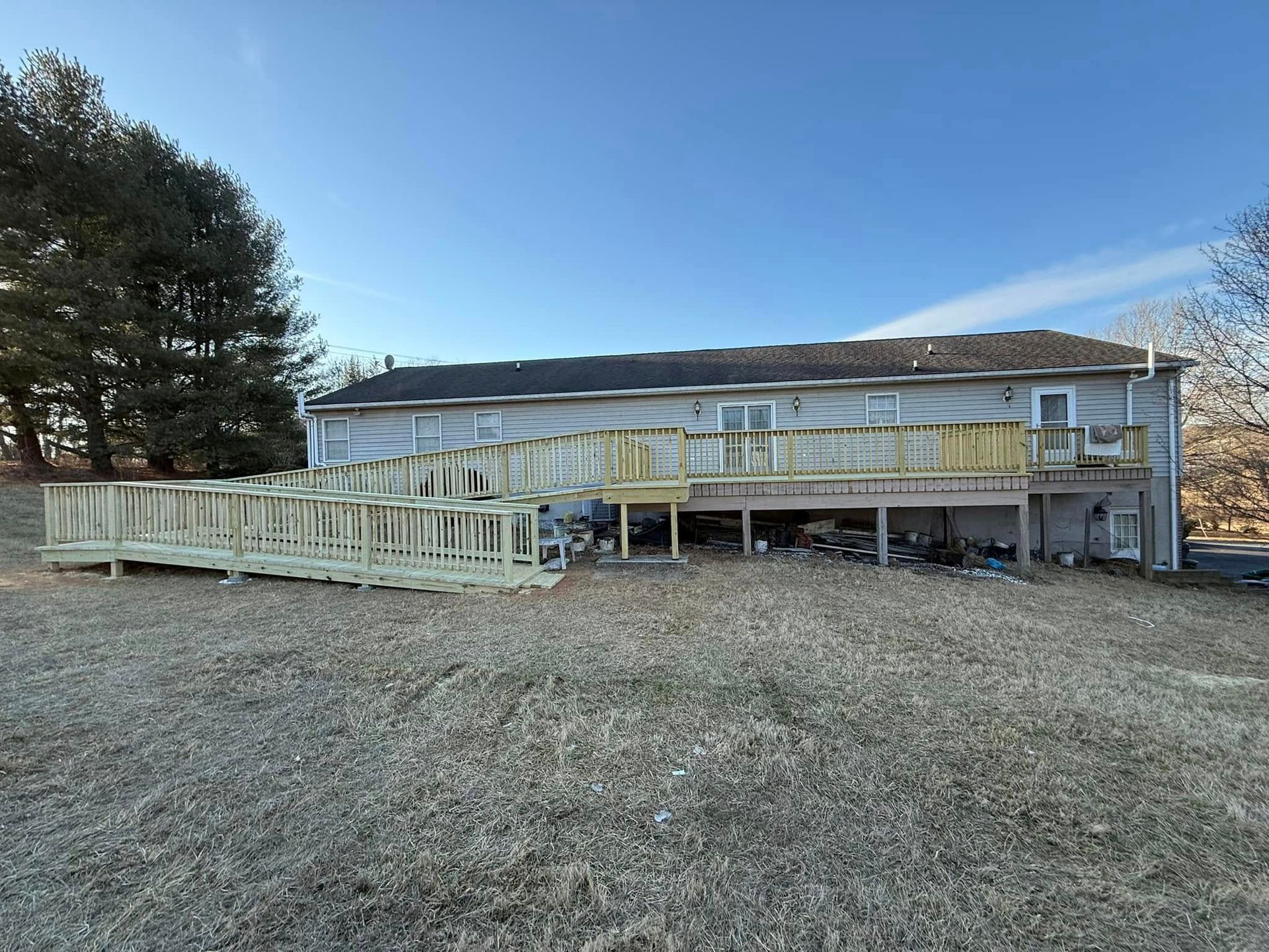 A long, wooden accessibility ramp with railings under construction along the back of a single-story house.