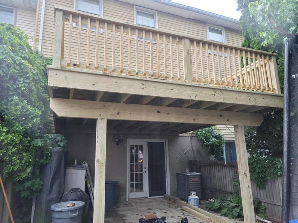 A newly constructed wooden deck attached to the second story of a tan house, featuring a patio space underneath.