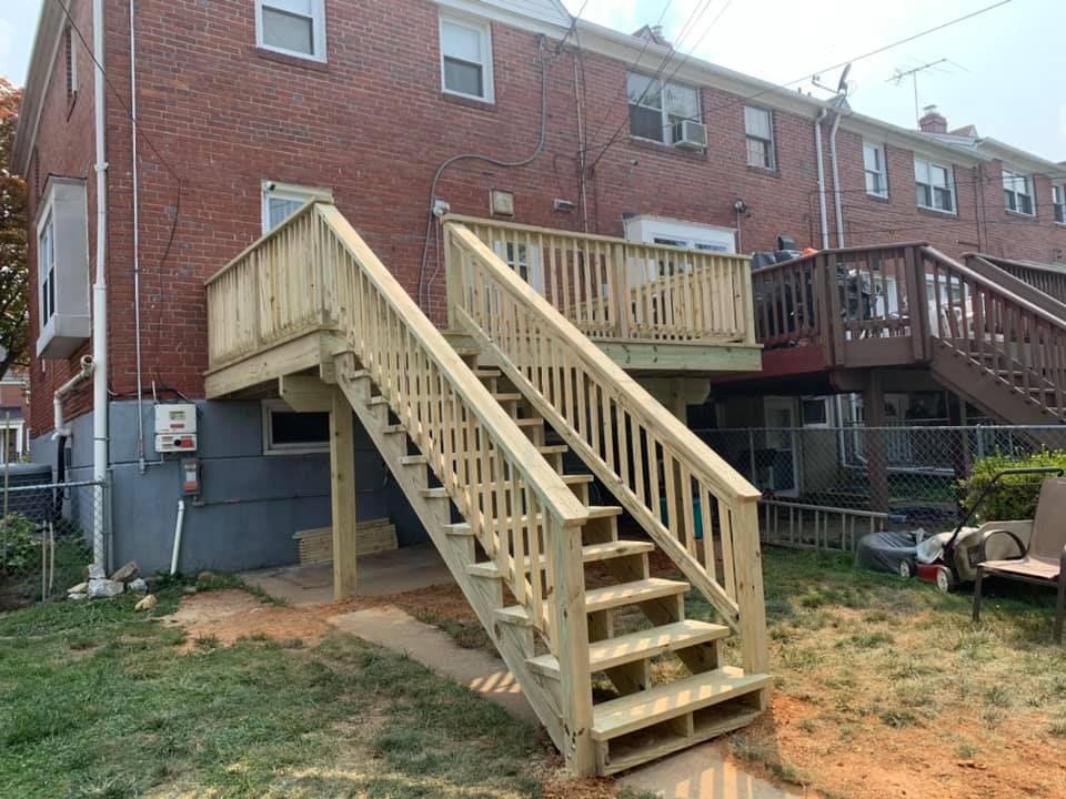 A newly constructed wooden deck and staircase attached to the rear of a multi-story red brick townhouse.