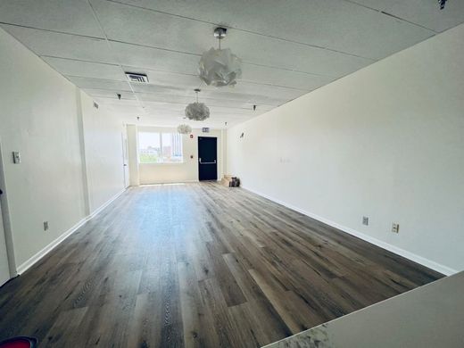 An empty, long rectangular room with light gray wood-look flooring, white walls, and three hanging dome pendant lights.