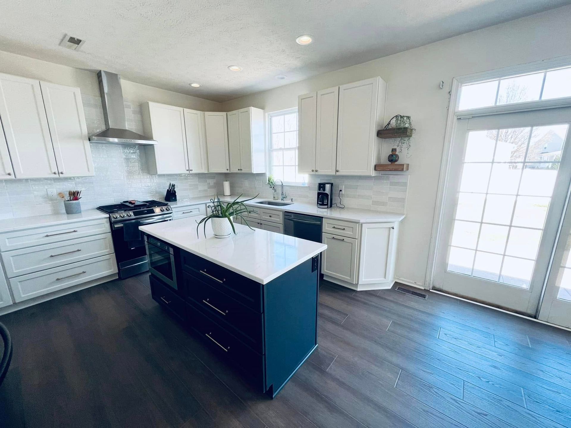 A modern kitchen with white cabinets, a dark blue center island with a white countertop, and wood-look flooring.