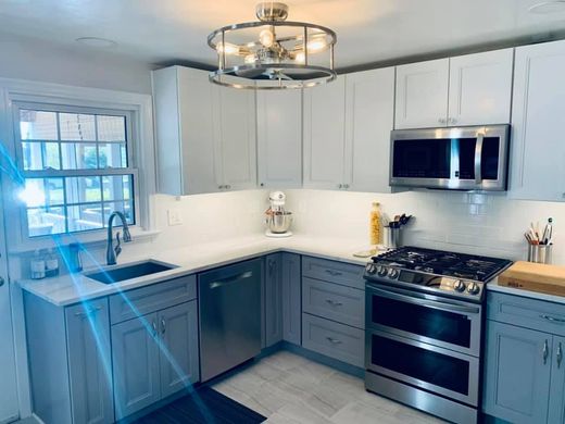 Modern kitchen with white upper cabinets, gray lower cabinets, stainless steel appliances, and a circular ceiling light.