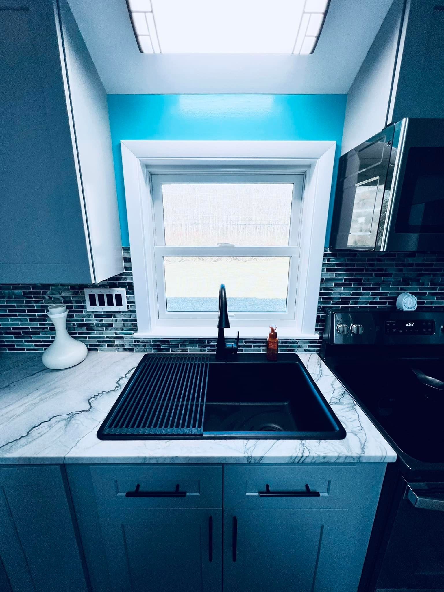 A kitchen sink area featuring a black basin, a dark faucet, marble-style countertops, and a bright blue wall by the window.
