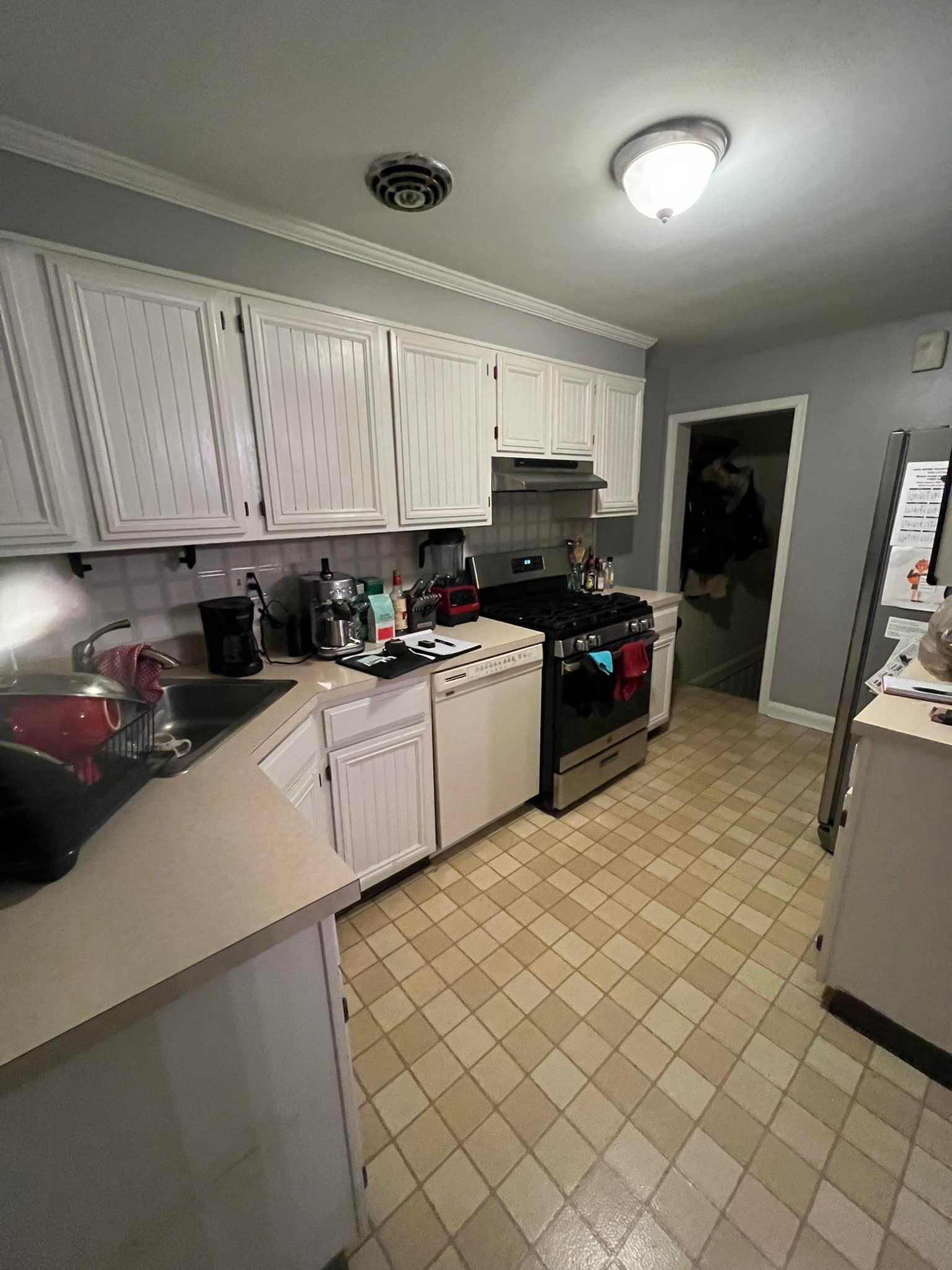 A kitchen with white cabinets, light-colored countertops, a gas stove, tiled floors, and gray walls.