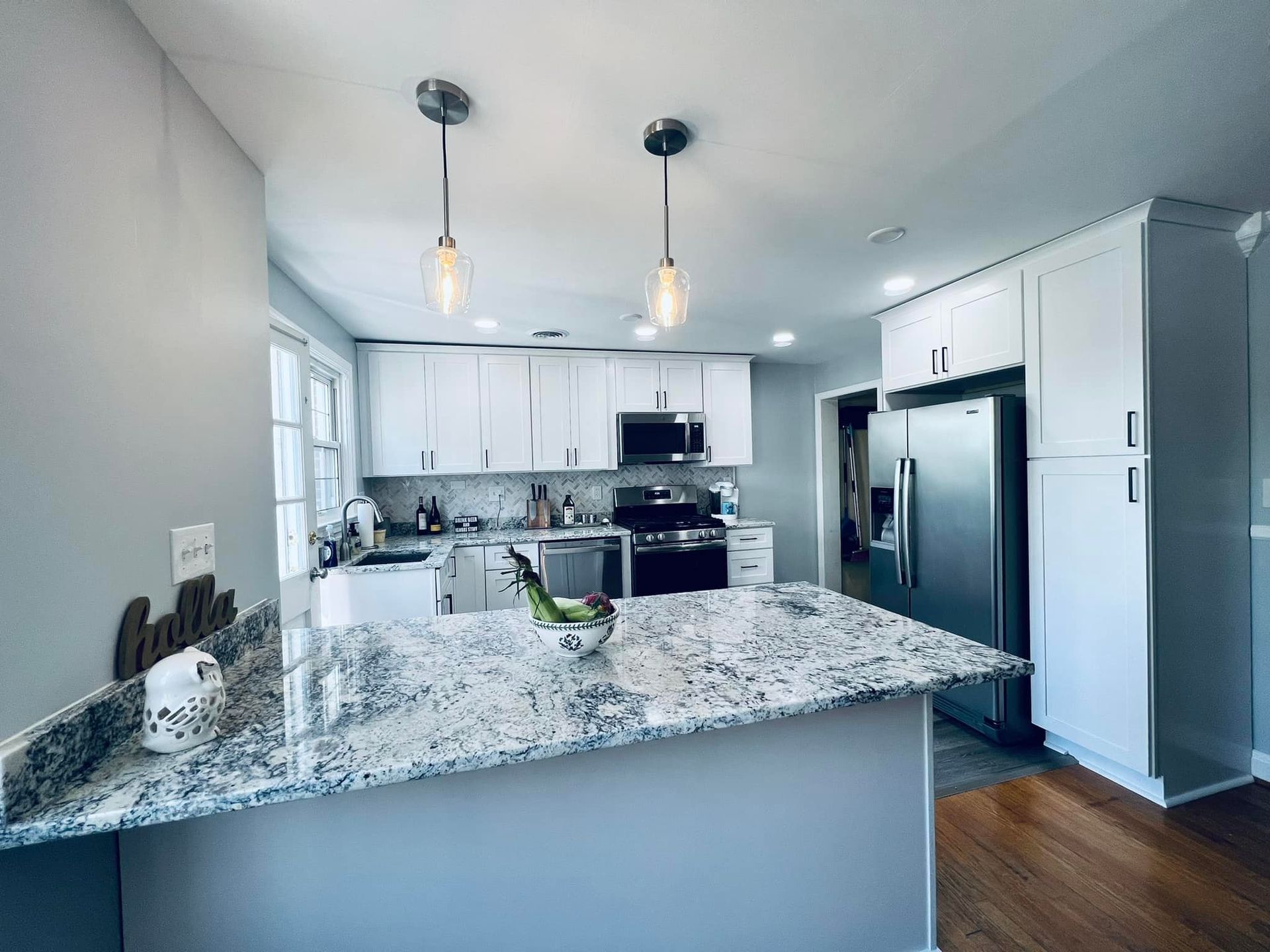 A modern kitchen featuring white cabinets, a granite island countertop, stainless steel appliances, and pendant lighting.