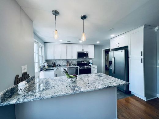 A modern kitchen featuring white cabinets, a granite island countertop, stainless steel appliances, and pendant lighting.