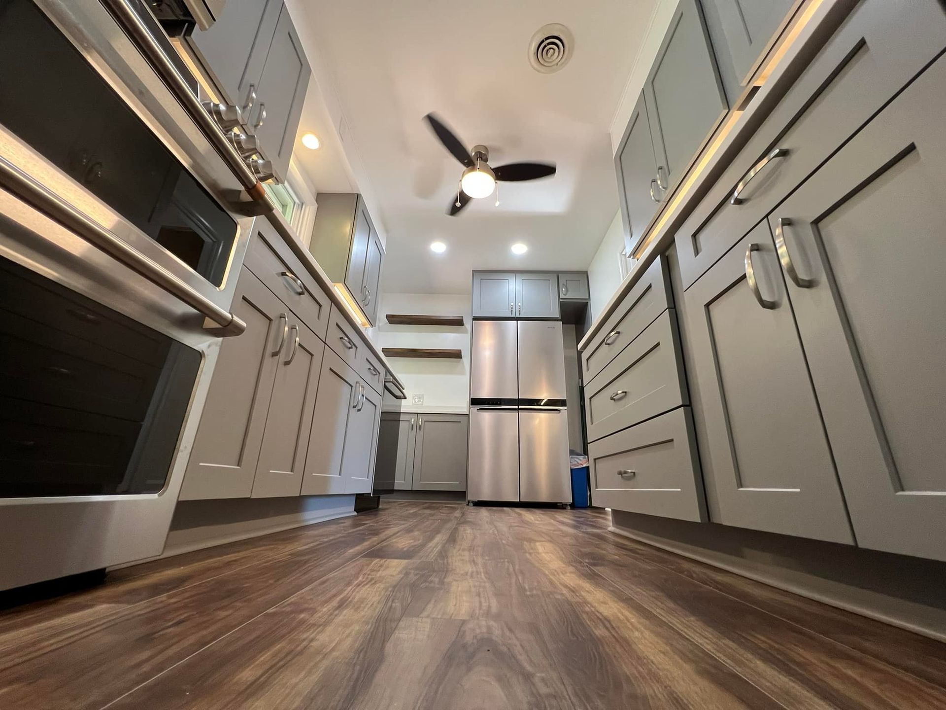 A low-angle view of a modern kitchen with grey cabinets, stainless steel appliances, and wood-look flooring.