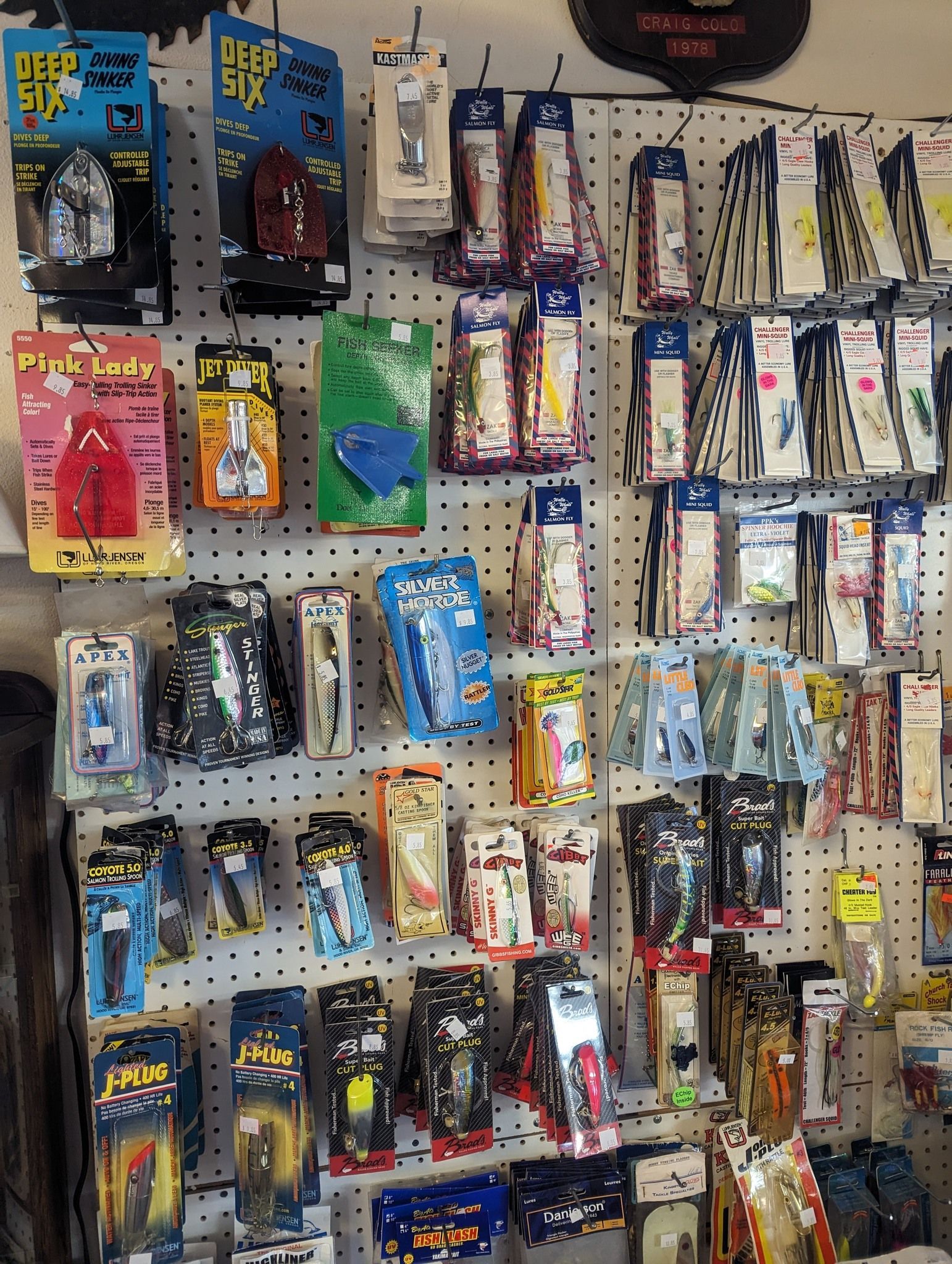 Fishing lures displayed on a pegboard wall, various colors and brands, in a store.