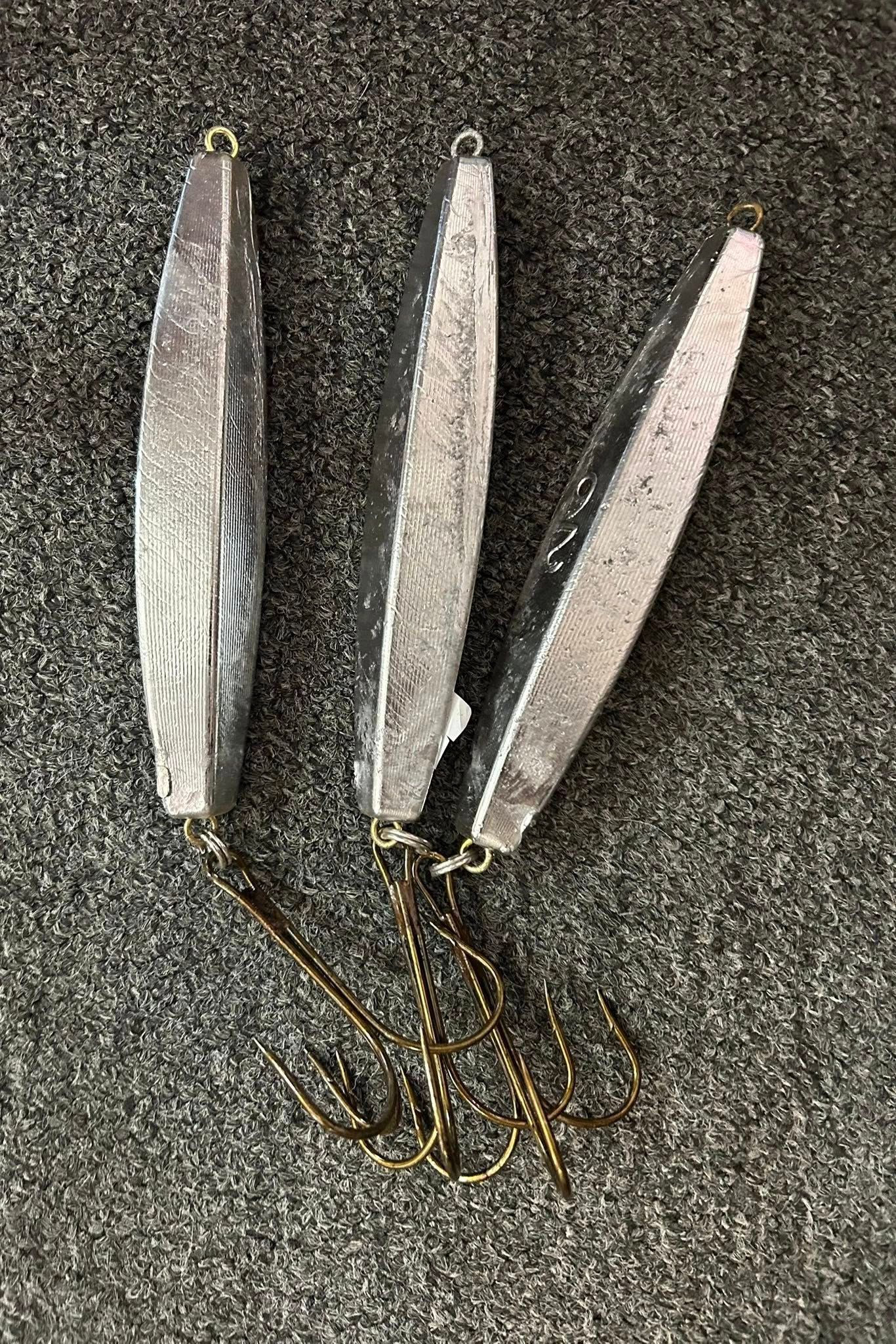 Three silver fishing lures with hooks on a textured surface.