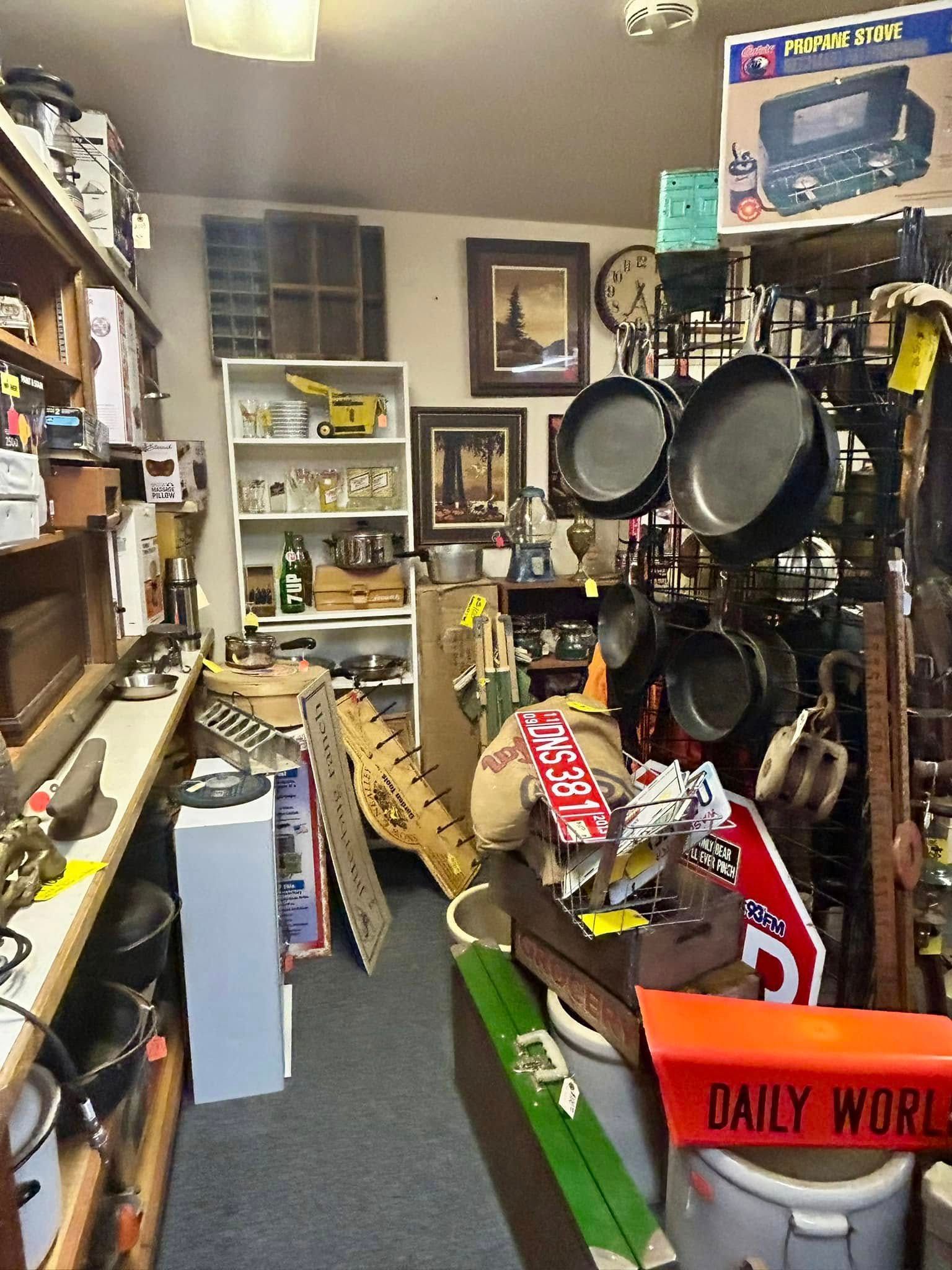 Antique store interior, overflowing with items. Cast iron pans hang. Shelves, tables, and walls are full.