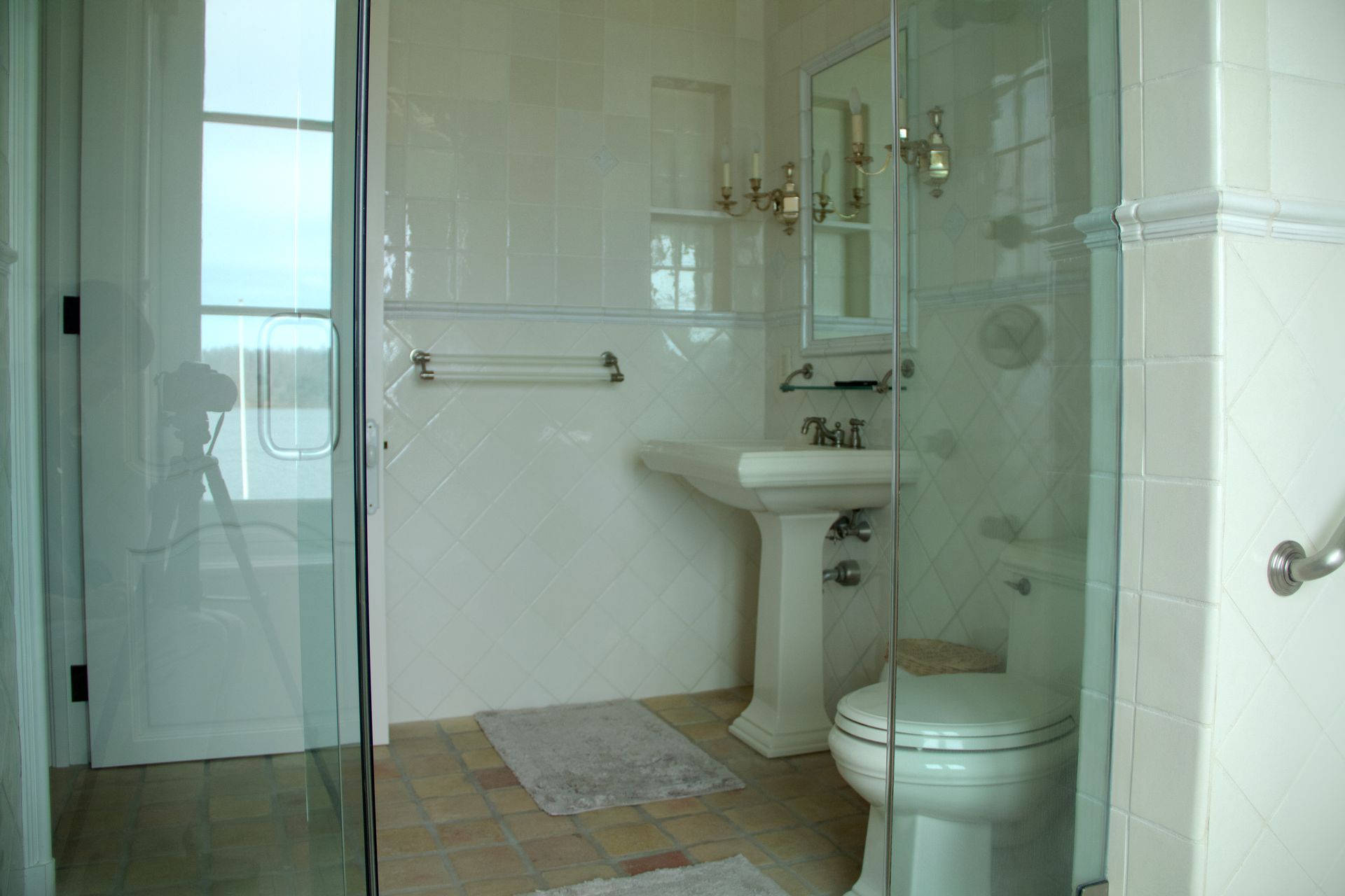 Bathroom with glass shower, pedestal sink, and toilet, all in shades of white and cream.