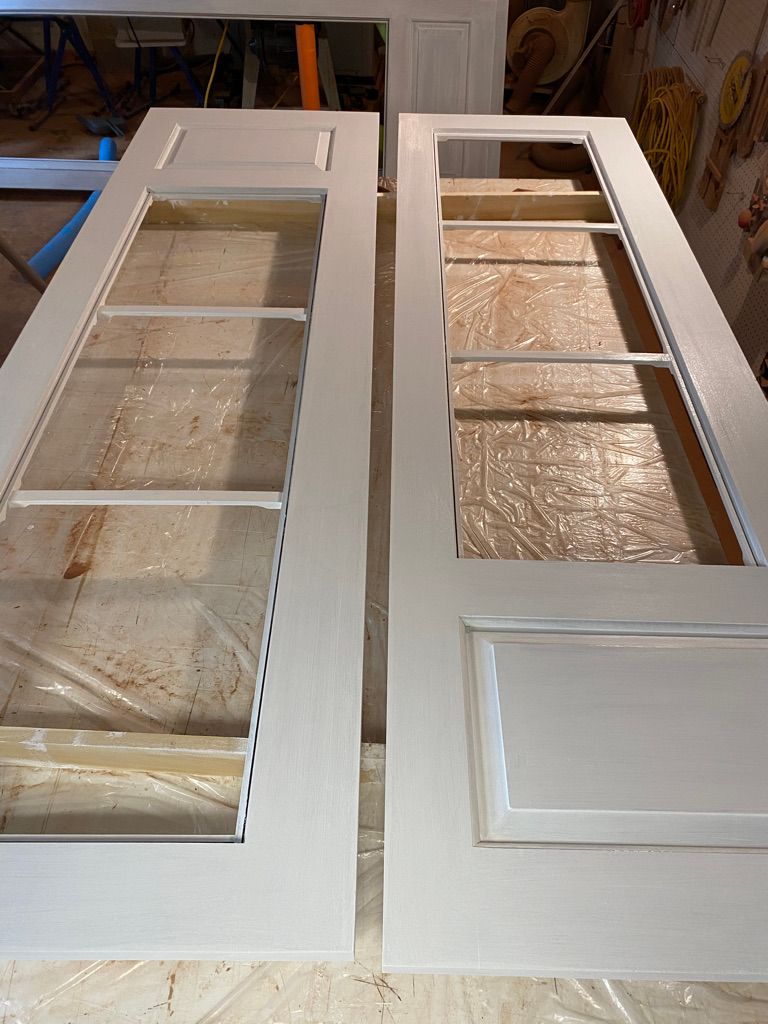 Two white-painted interior doors with glass panels, lying on a work surface.
