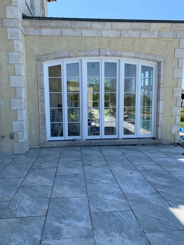 White folding glass doors on a patio with gray pavers and a light yellow stucco wall with stone trim.